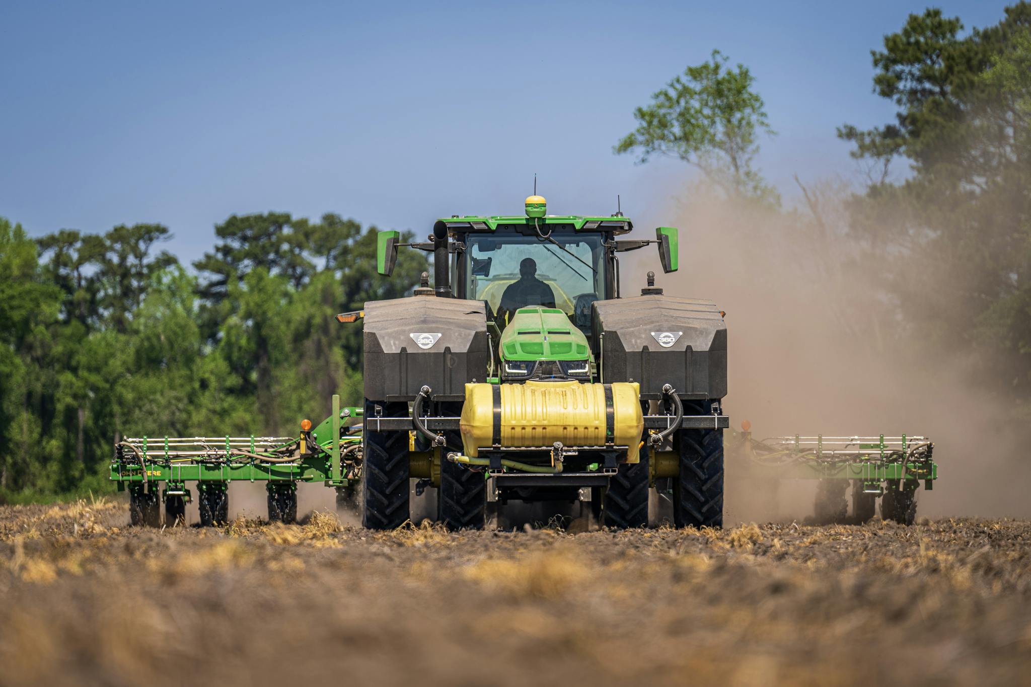 A green tractor in use for sowing on a sunny rural farm field in summer.